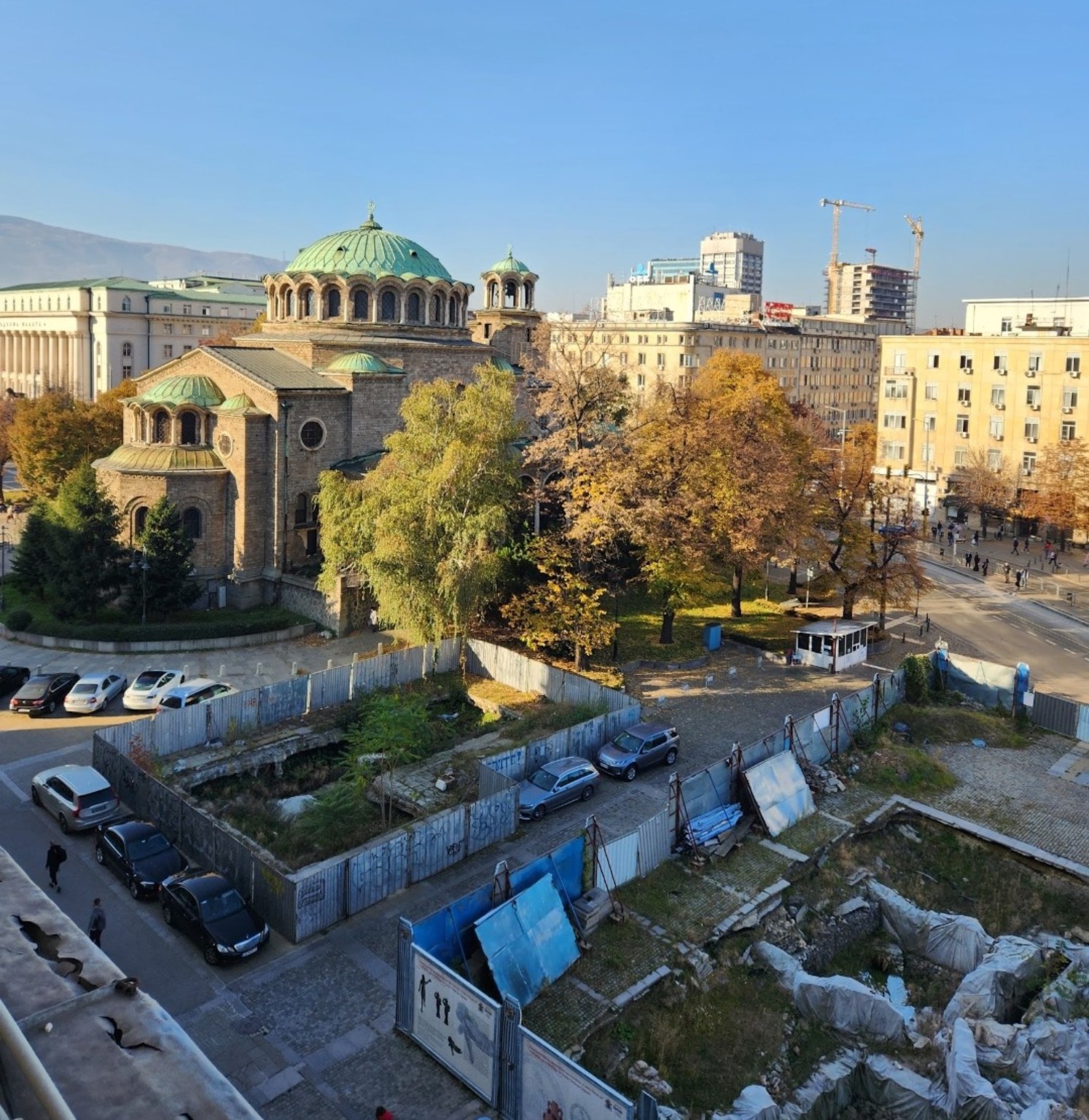 Historic cathedral with green domes beside archaeological remains and modern city buildings in Sofia, Bulgaria