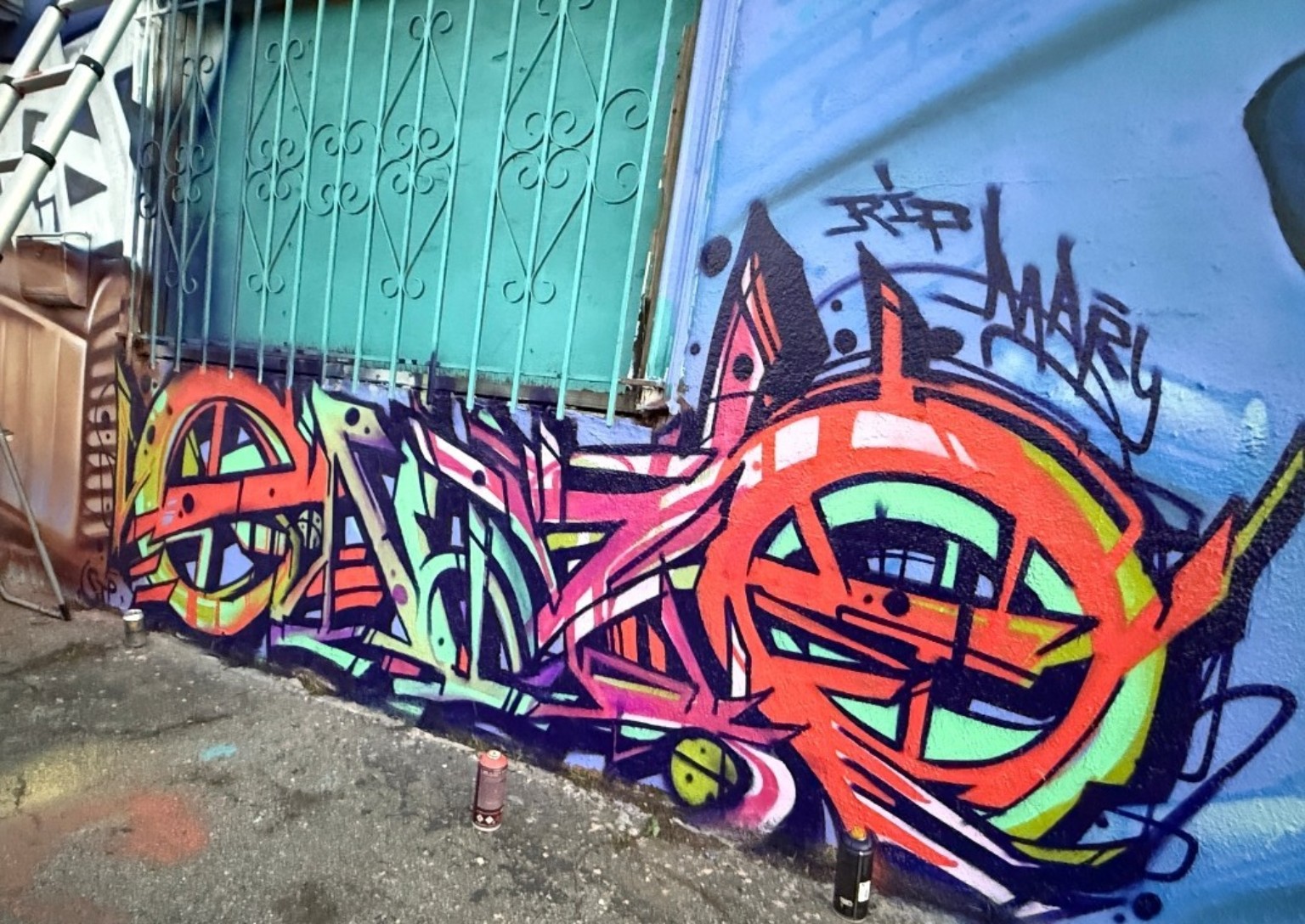 Colorful graffiti lettering with bold orange, green and purple shapes painted beside a turquoise gate