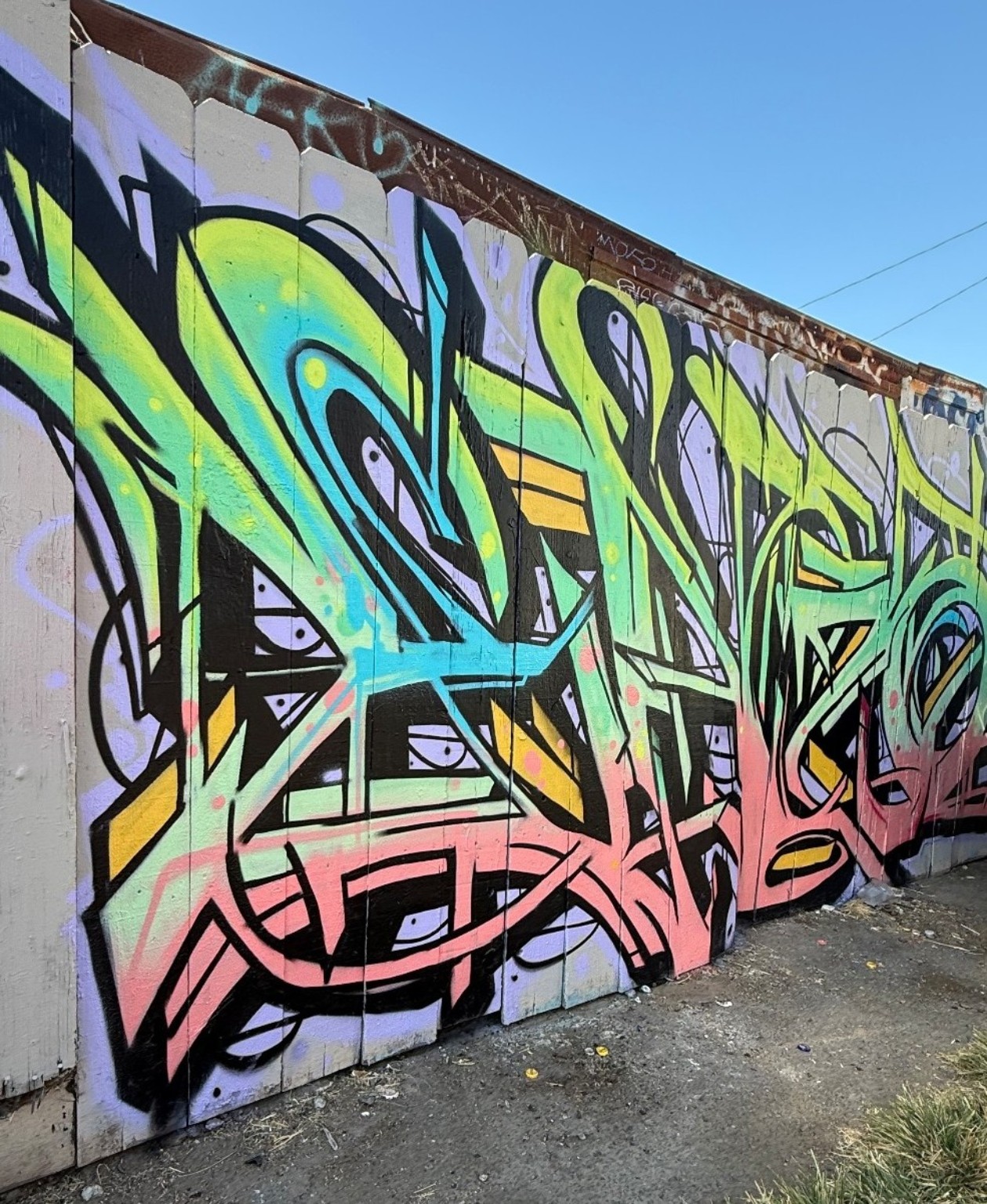 Detailed graffiti lettering painted in lime green, turquoise and pastel pink on an outdoor fence