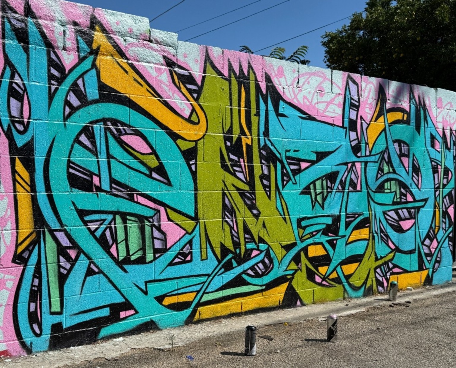 Wide colorful graffiti mural with turquoise, lime, yellow and pink lettering on a concrete block wall