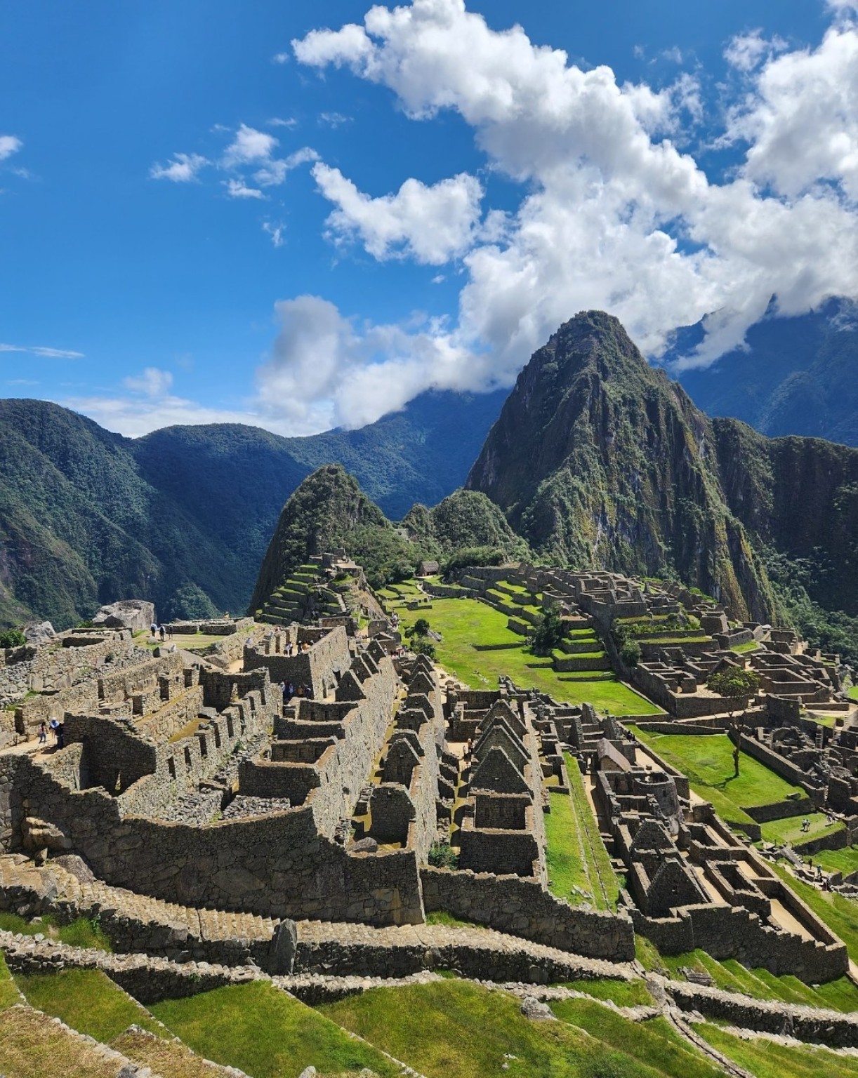 Machu Picchu stone terraces and buildings framed by Andean mountains beneath clouds